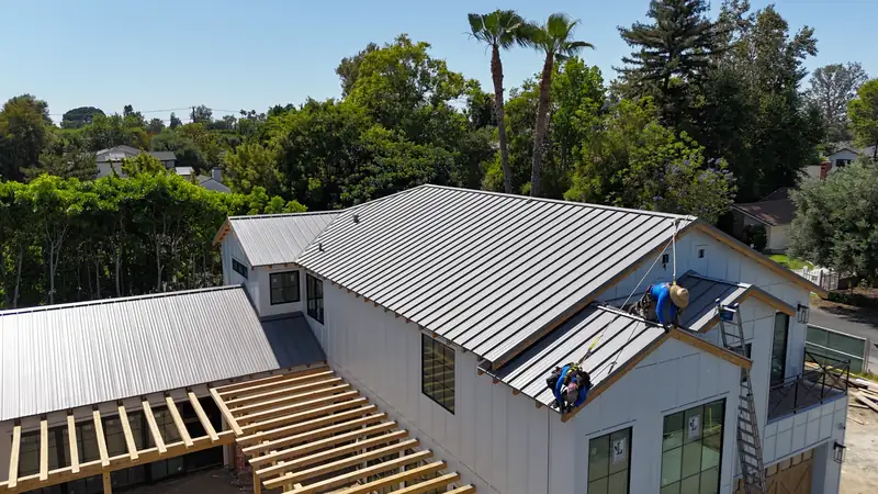Our crew installing gray standing seam panels on a white board-and-batten house