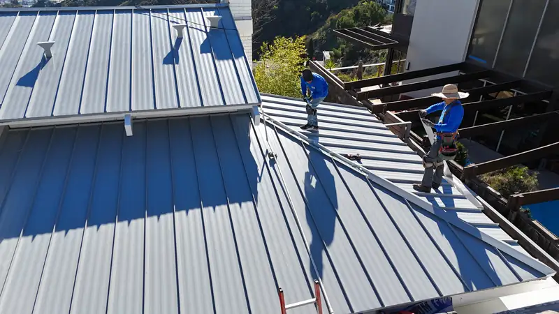 Two Eclipse crew members trimming the hip of a light gray standing seam roof on a Los Angeles hillside house