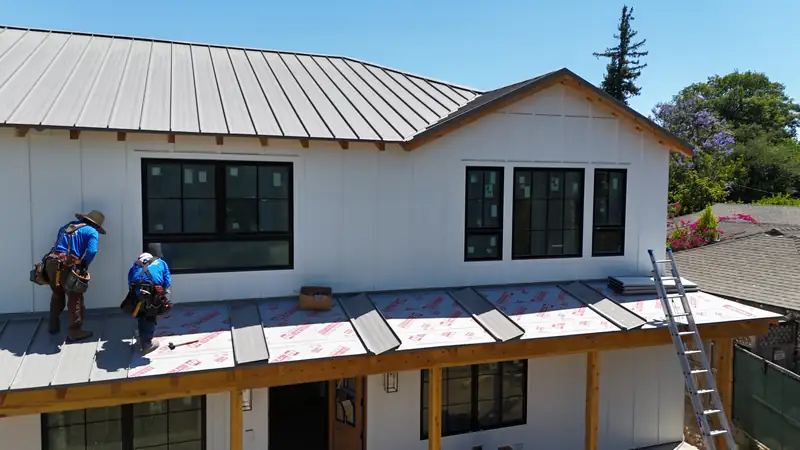 Roofers fastening panels over red high-temperature underlayment at the eave